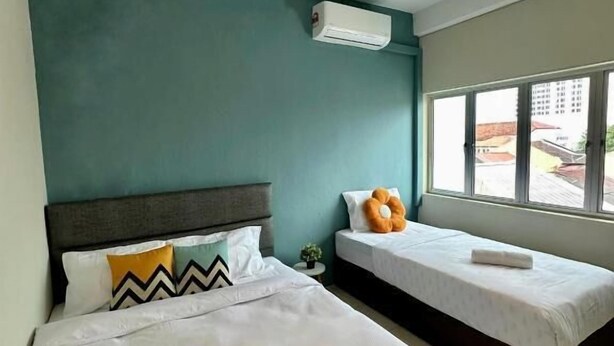 A hotel room with two beds, teal walls, an air conditioning unit, and a window with a view of buildings. - Swing & Pillows at Penang Road (George Town)