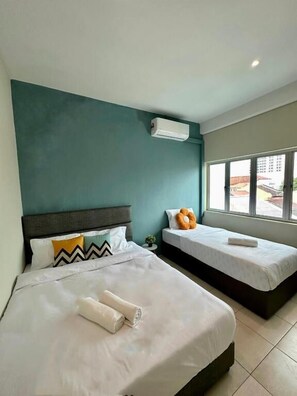 A hotel room with two beds, teal walls, an air conditioning unit, and a window with a view of buildings. - Swing & Pillows at Penang Road (George Town)