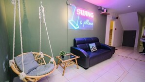 A room with a hanging swing chair, a black sofa, and a neon sign reading "SWING & pillows". - Swing & Pillows at Penang Road (George Town)