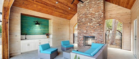 A spacious indoor patio with a brick fireplace, wooden ceiling, and a ceiling fan.