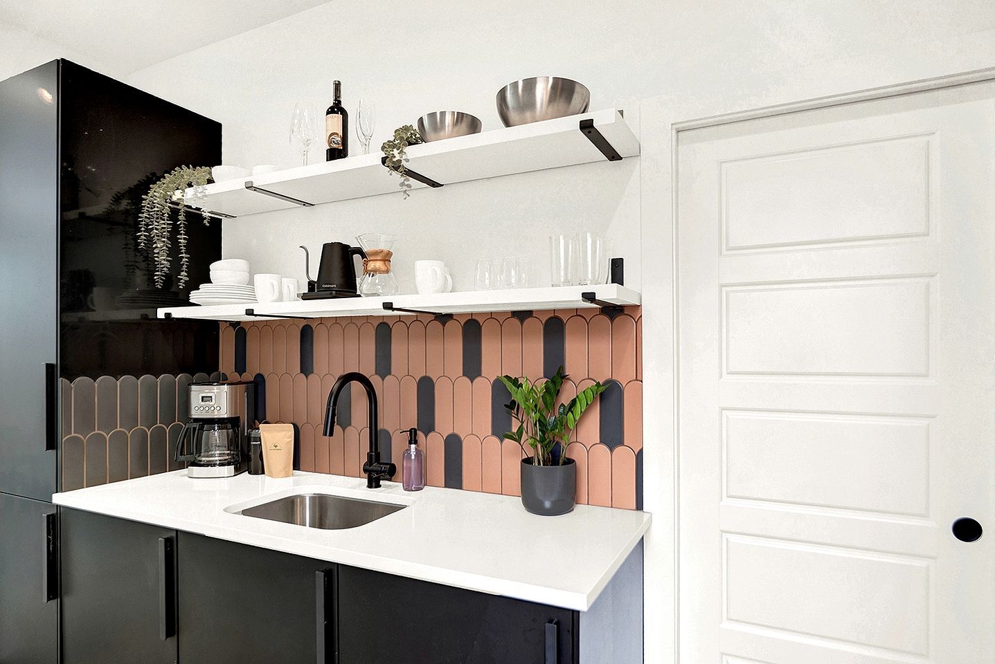 Une cuisine moderne avec un plan de travail blanc, des meubles noirs, une machine à café, un évier et une plante en pot.