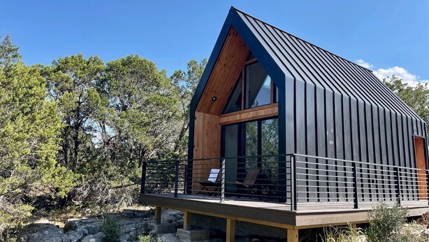 Eine moderne Hütte mit geneigtem Dach, großen Fenstern und einer Holzterrasse.