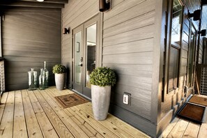 Une terrasse en bois avec une porte, des plantes en pot et un paillasson.