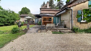 Un bâtiment de style rustique avec une allée en gravier, un espace extérieur aménagé pour s’asseoir et un coin bar.