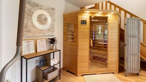 Un sauna en bois doté d’une porte en verre, une étagère en bois ornée d’affiches sur le yoga et l’entraînement croisé, et une étagère en osier.