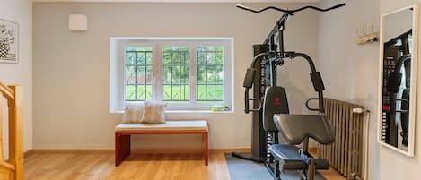 A gym with exercise equipment, a bench, and a window with a view of greenery.