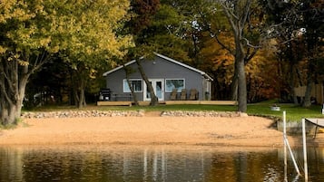 A lakeside cabin with a dock, surrounded by trees and a sandy beach.