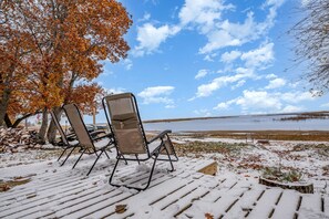 Une terrasse enneigée avec des chaises d’extérieur, un arbre aux feuilles d’automne et une vue sur un lac.
