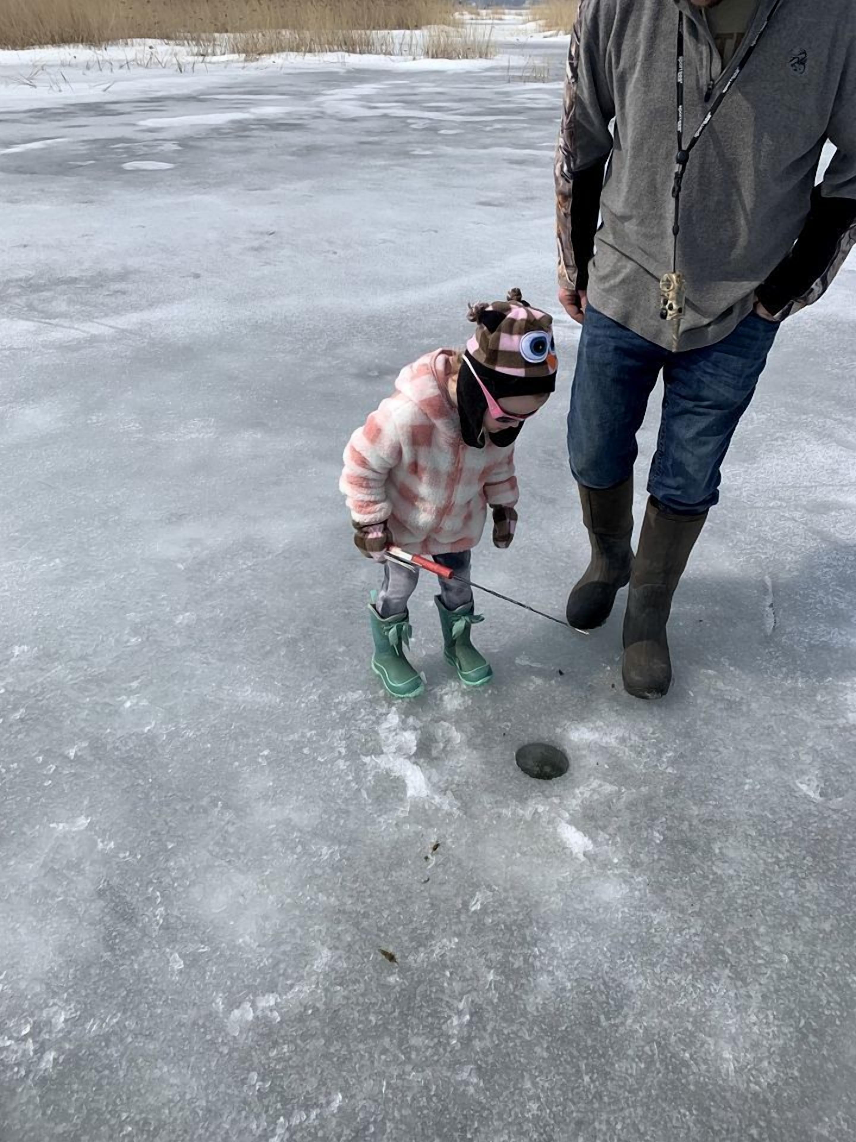 Un niño con un conjunto rosa y marrón está de pie sobre hielo, con un hombre cerca.