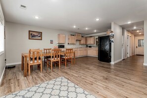 A modern kitchen with wooden cabinets, a black refrigerator, and a dining area with wooden chairs.