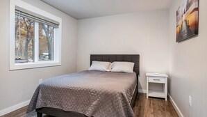 A bedroom with a bed, a nightstand, a window with blinds, and a painting on the wall.