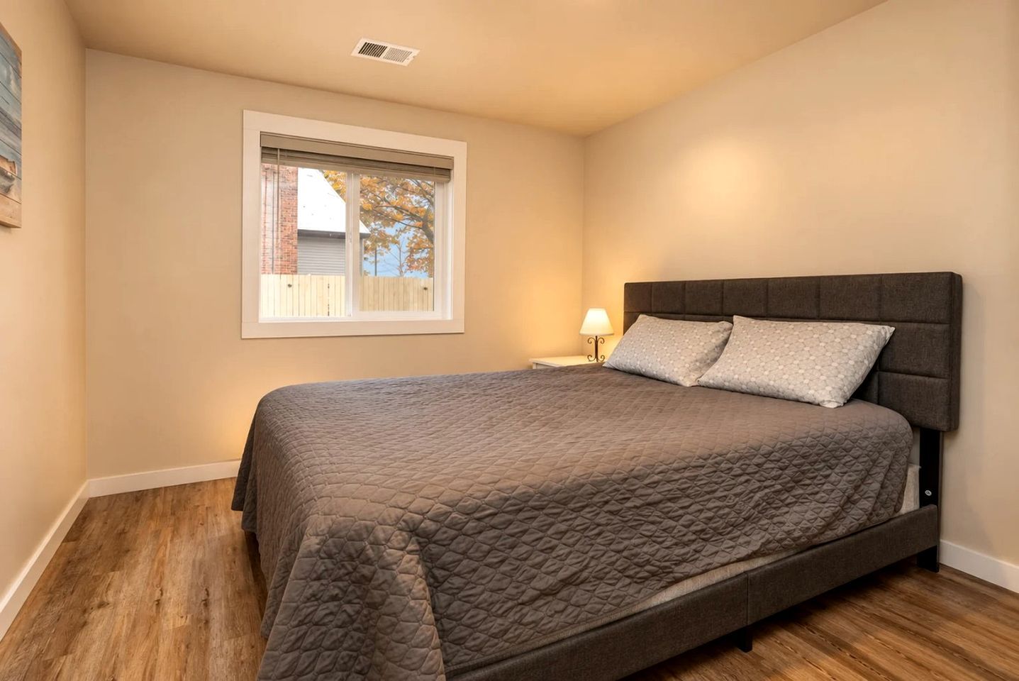Un dormitorio con cama, ventana y mesita de noche con lámpara.