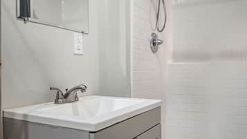 A bathroom with a white sink, a mirror, a shower with a handheld showerhead, and a tiled wall.