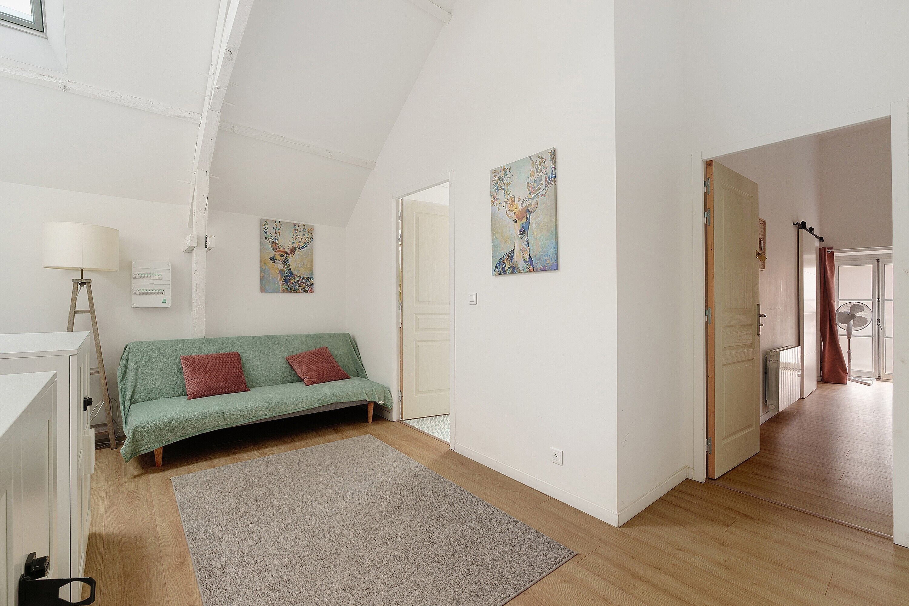 A room with a green sofa, a white lamp, and two paintings on the wall.