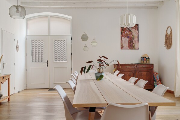 A dining area with a long table, chairs, a wooden cabinet, and a door with decorative glass panels.