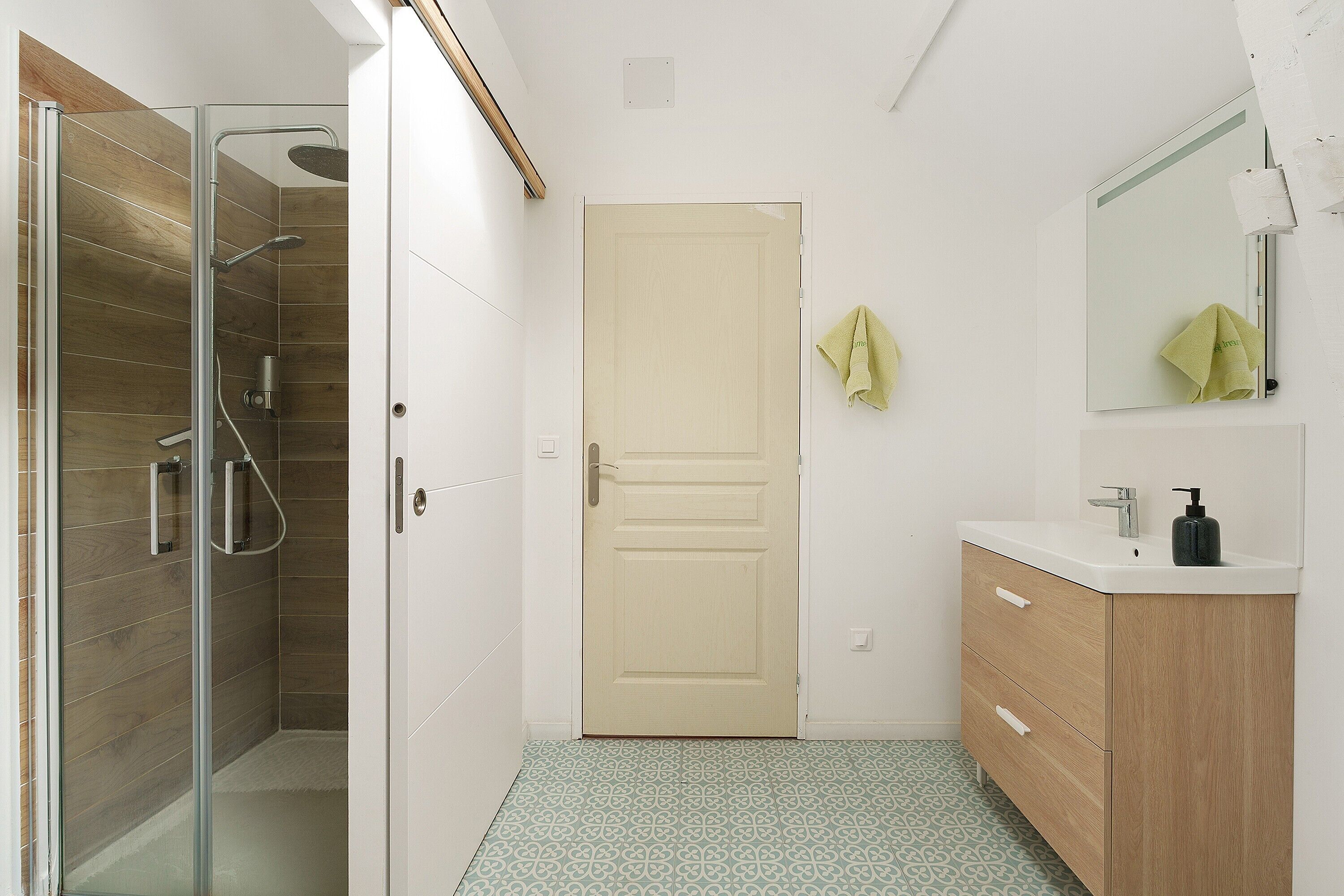 Une salle de bain avec une douche à parois de verre, un meuble-lavabo en bois, un lavabo avec un miroir et des carreaux de sol à motifs.