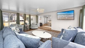 Ein geräumiges Wohnzimmer mit grauen Sofas, einem runden Couchtisch und einem Deckenventilator.