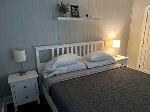 A bedroom with a bed, two bedside tables, a nightstand, a wall-mounted shelf with a sign, and a door. - Riverfront Cottage with Barbecue, Kayaks and Dock in Charlotte, North Carolina (Charlotte)
