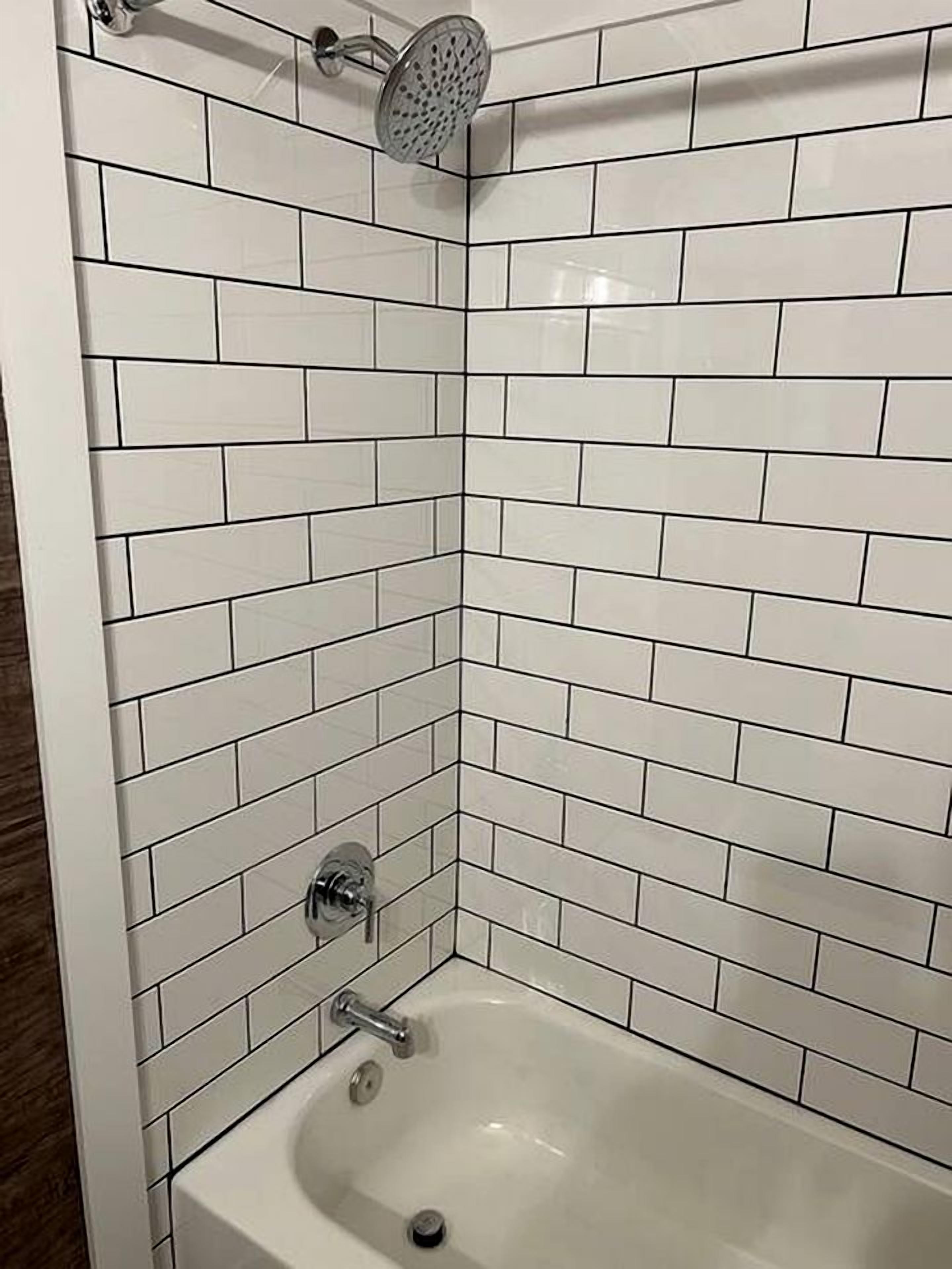 A corner bathroom with white subway tiles, a showerhead, and a bathtub.