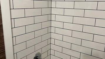 A corner bathroom with white subway tiles, a showerhead, and a bathtub.