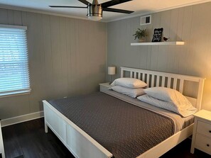 Un dormitorio con cama, mesita de noche, estante en la pared y ventilador de techo.
