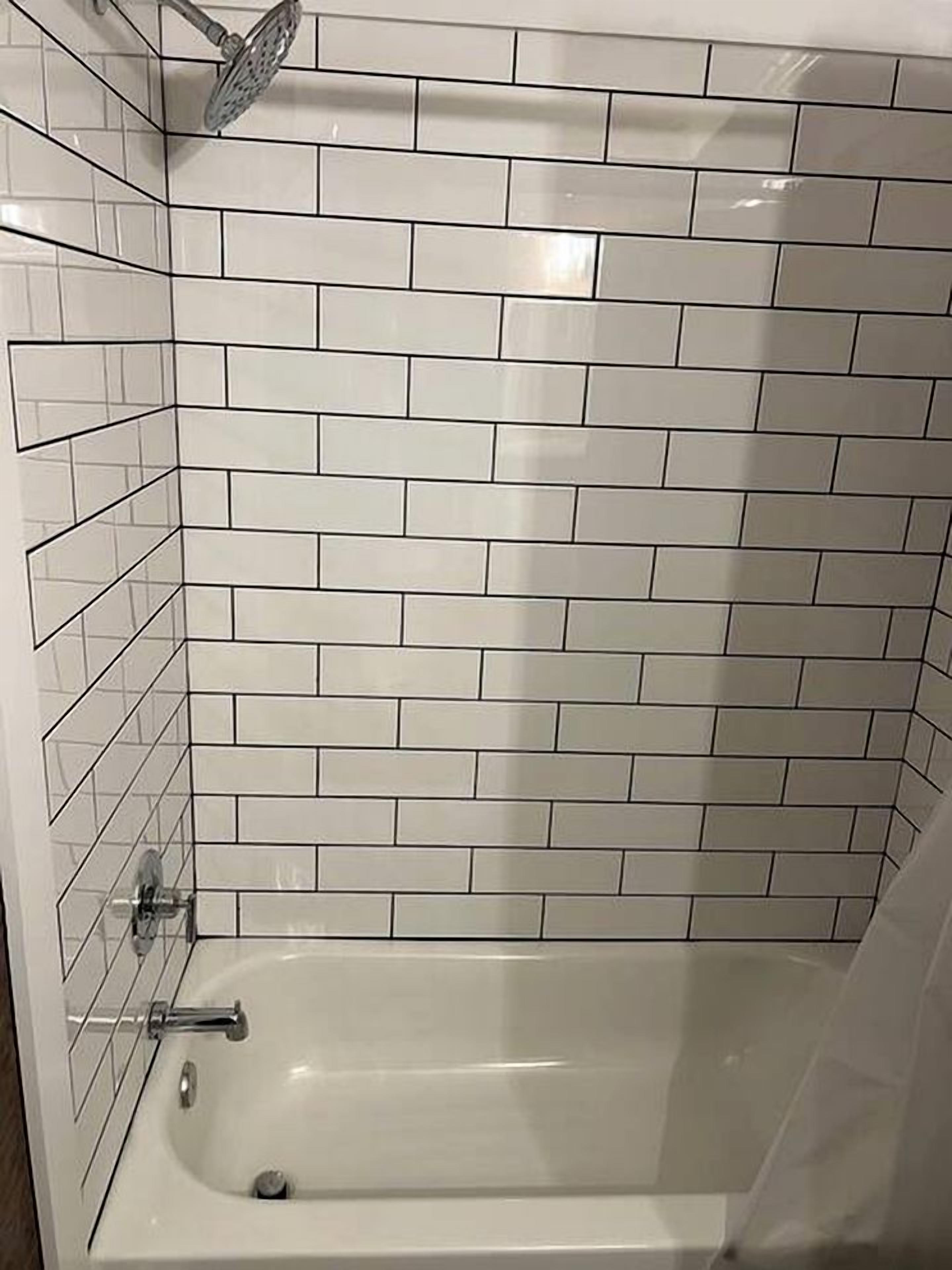 Une salle de bain avec des carreaux de céramique blancs rectangulaires, une baignoire et une pomme de douche.