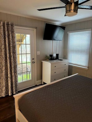 A bedroom with a bed, a dresser, a ceiling fan, a TV, and a window with blinds. - Riverfront Cottage with Barbecue, Kayaks and Dock in Charlotte, North Carolina (Charlotte)