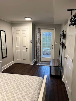 Une chambre à coucher avec un lit, une porte, un miroir, une armoire et une vue sur l’extérieur, visible à travers la porte.