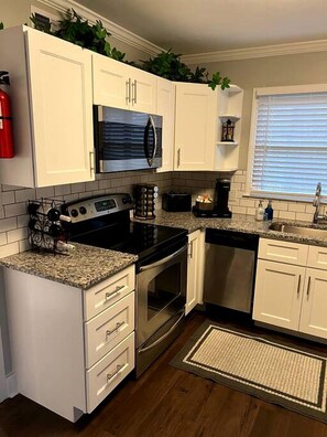 A kitchen with white cabinets, a stainless steel stove, a microwave, and a window with blinds.