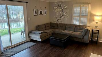 A living room with a sectional sofa, a coffee table, a side table with a lamp, and a decorative tree light.