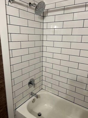 A corner bathroom with white subway tiles, a showerhead, and a bathtub.