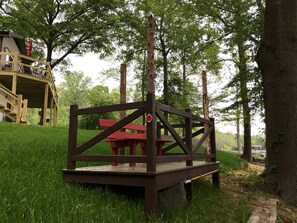 A wooden deck with a picnic table and a red sign, surrounded by trees.