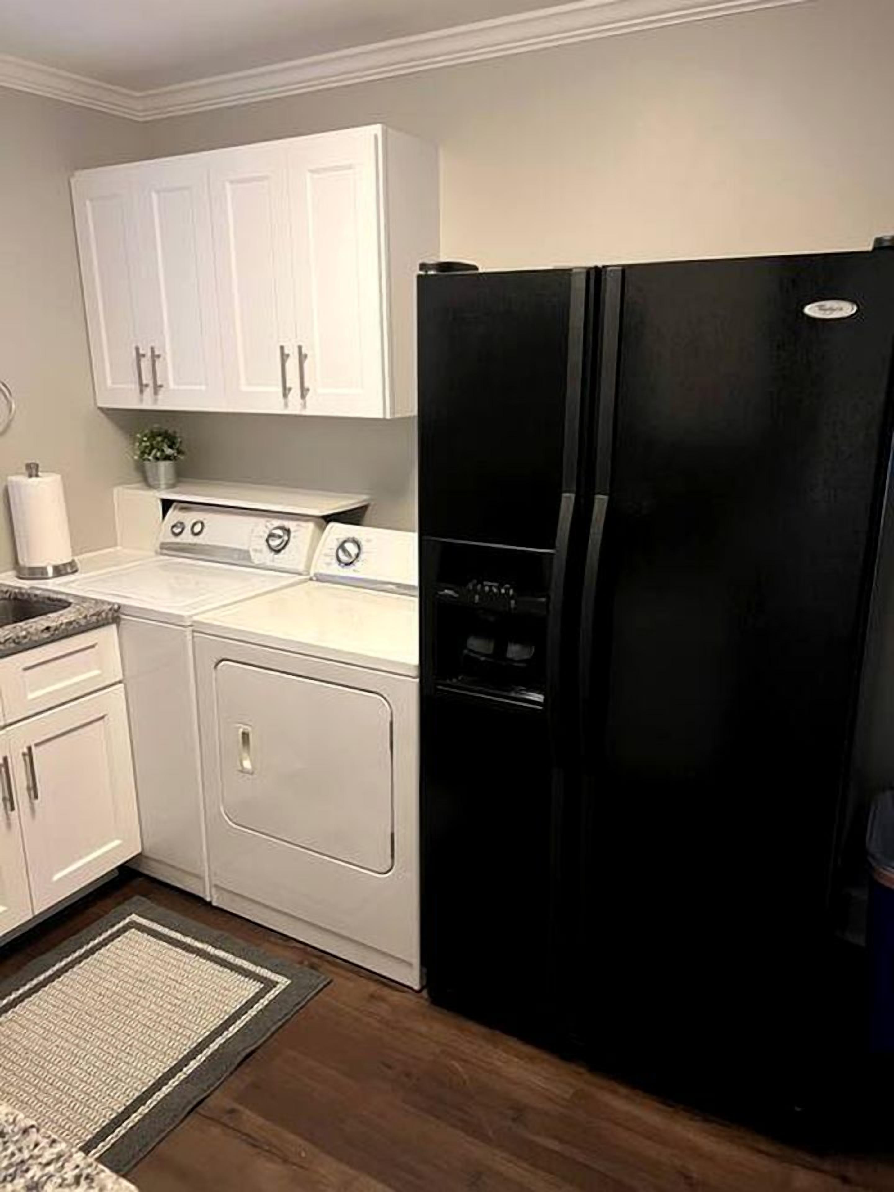A kitchen with white cabinets, a black refrigerator, a stove, and a washing machine.