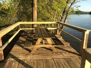 A wooden deck with a picnic table and railings, overlooking a body of water.