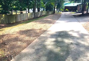 A concrete pathway leading to a building with a green roof, surrounded by trees and a wooden fence.