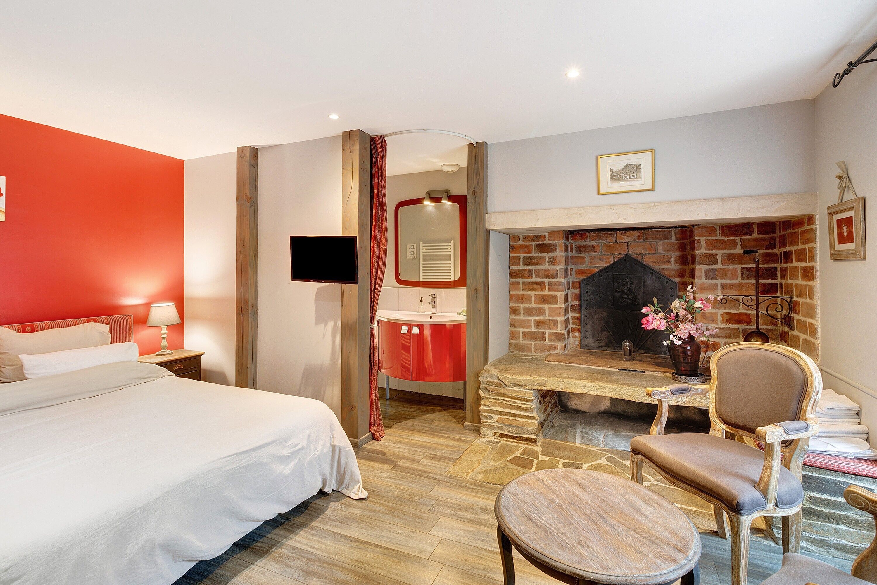 Une chambre d’hôtel avec un lit, une cheminée, une télévision et une salle de bain visible à travers une porte ouverte.