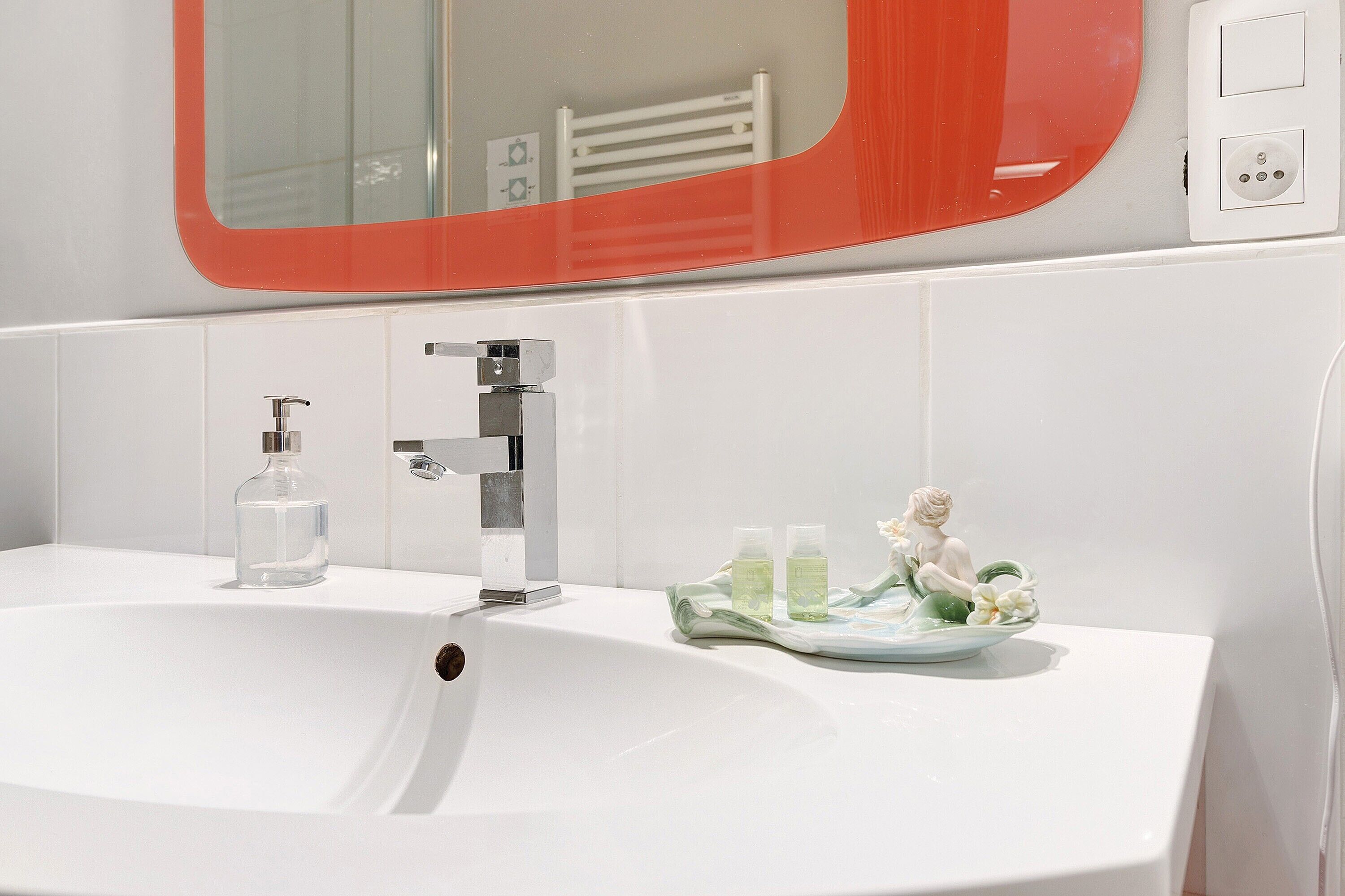 Une salle de bain avec un lavabo blanc, un miroir avec un cadre rouge et un porte-serviettes.