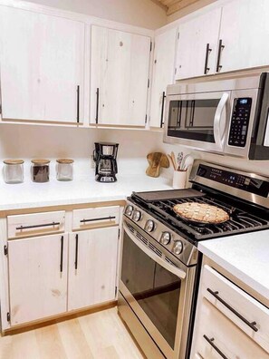 Una cocina con gabinetes blancos, microondas, estufa y cafetera.