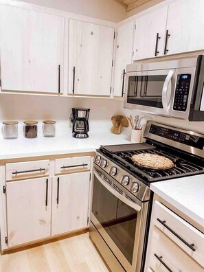 A kitchen with white cabinets, a microwave, a stove, and a coffee maker. - Cabin Charm by the Pine: Pet-Friendly Retreat in Mission Township's Riverside Haven (Mission Township)