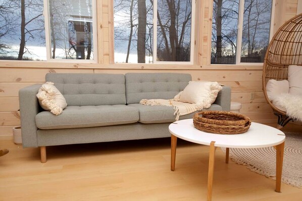 A room with a grey sofa, a round white table, a wicker basket, and a wicker chair.