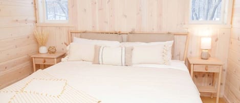 Une chambre de style cabane en bois, avec un lit, deux tables de chevet et une fenêtre.