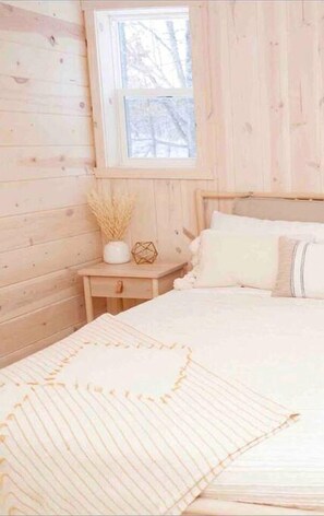 A wooden room with a bed, a nightstand, and a window.