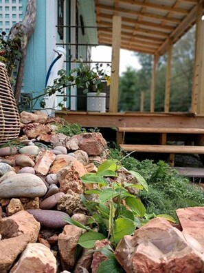Een tuin met een houten terras, diverse planten en een stenen muur.