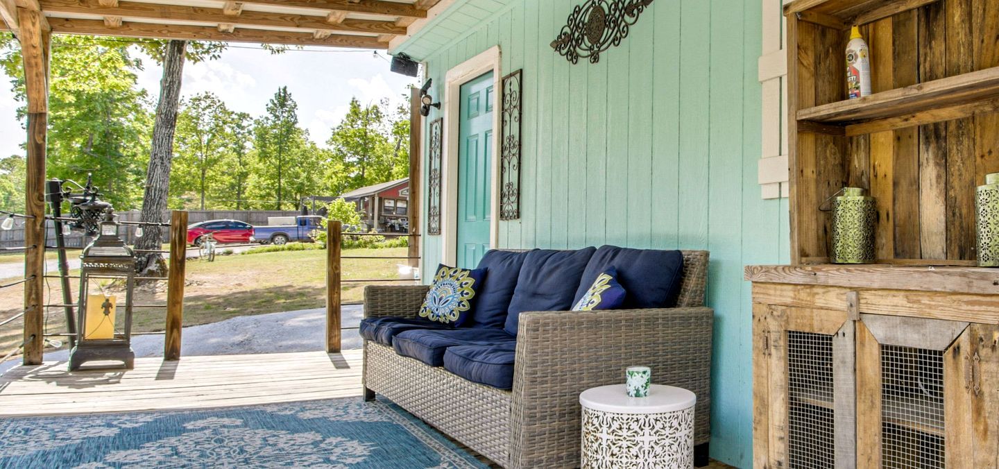 A covered porch with a wicker sofa, a small round table, and a decorative lantern.