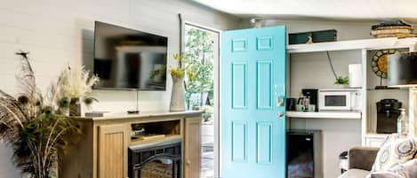 A compact living space with a television, a teal door, a coffee machine, and a microwave.