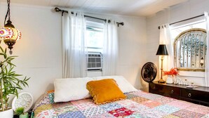 A bedroom with a bed, a bedside table, a lamp, a mirror, and a window with curtains. - Sweet Tiny House Perfect for a Romantic Retreat in Alabama (Rogersville)