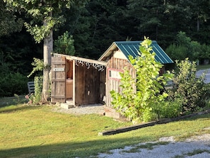 A rustic wooden cabin with a green roof, a small porch, and a sign indicating it is a camping area.