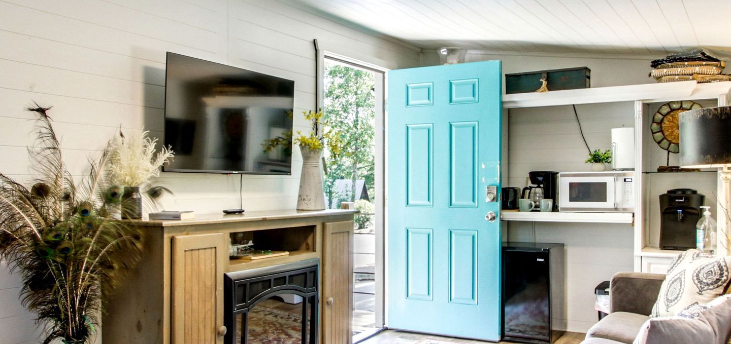 Un espacio habitable pequeño con televisión, una puerta color turquesa, una cafetera y un microondas.