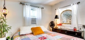 A bedroom with a bed, a bedside table, a lamp, a mirror, and a window with curtains.
