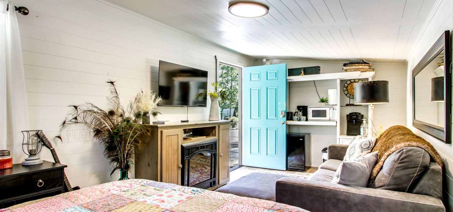 Un dormitorio con cama, cómoda, televisor, puerta azul y kitchenette.